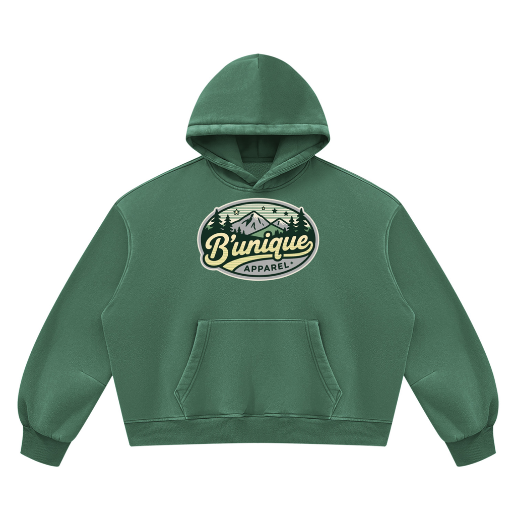Green ODMPOD Unisex UNIQUE MOUTAIN Vintage Wash Boxy Fleece Hoodie featuring a front kangaroo pocket and a circular chest graphic of mountains, pine trees, and the text Bunique APPAREL.