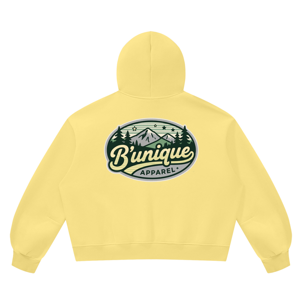 Light yellow Unisex UNIQUE MOUTAIN Vintage Wash Boxy Fleece Hoodie featuring a graphic on the back of mountains and pine trees inside an oval frame with the text Bunique Apparel.
