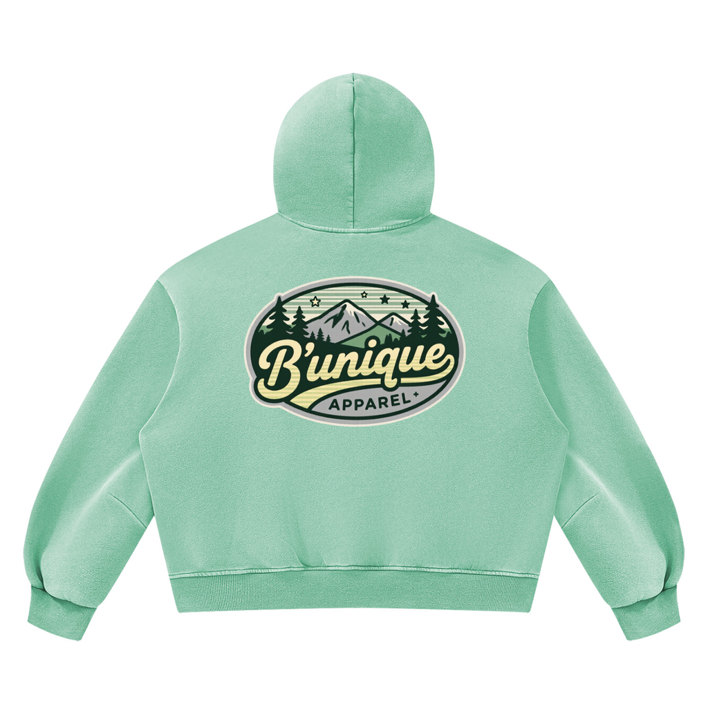 Back view of a light green Unisex UNIQUE MOUTAIN Vintage Wash Boxy Fleece Hoodie featuring a mountain landscape graphic with the text Bunique Apparel in an oval frame.
